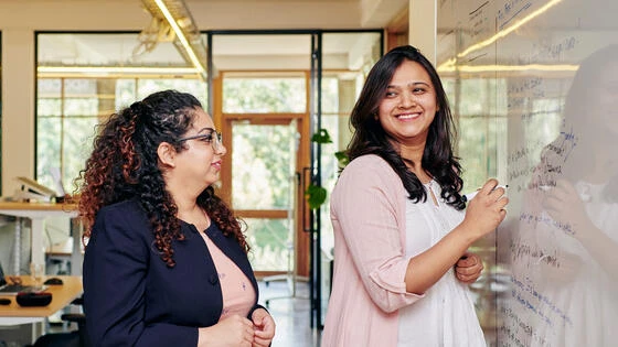 Two Deakin master of education leadership and learning student teachers talk in front of white board on campus.