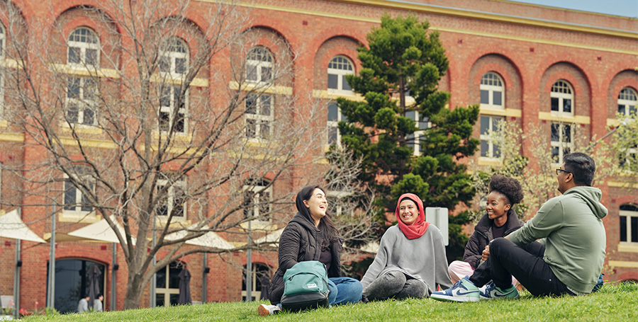 Four students sit on the grass and laugh at Waterfront campus