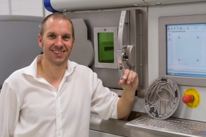 Dr Paul Collins with the drink bottle holder and the 3D titanium printer that created it.