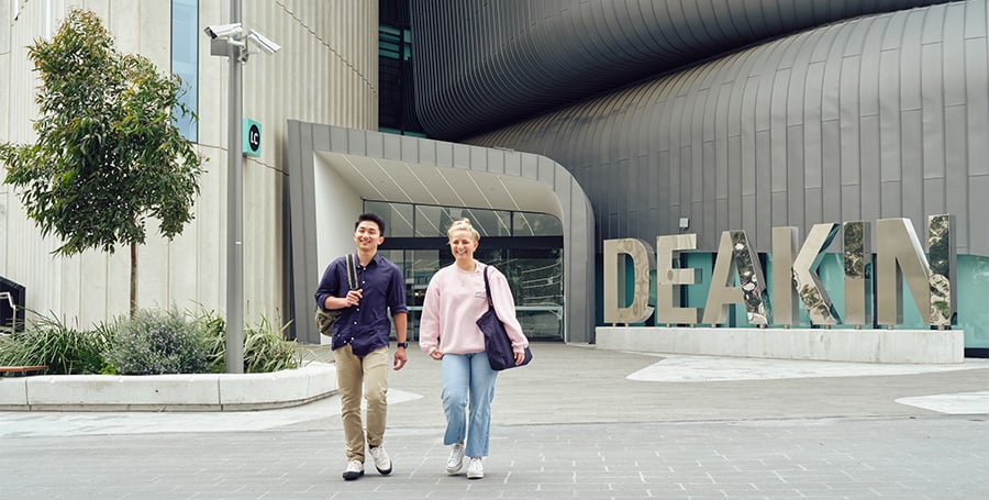 Two students walk outside in front of a Deakin sign at Burwood