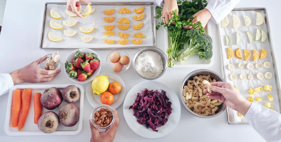 A table of colourful raw food in a lab with hands reaching in.