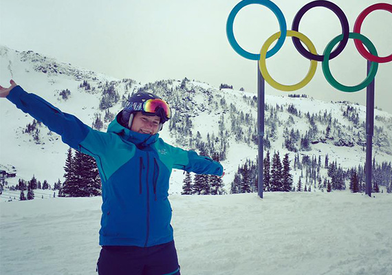 Young woman wearing snow clothing on the ski slopes in front of the Olympic rings 