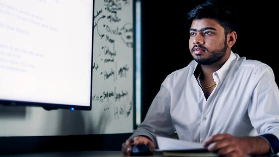 Deakin master of data science professional student sits at table with large computer on campus.