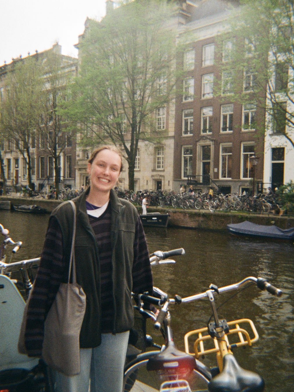 Student standing in front of bikes and a river in Amsterdam