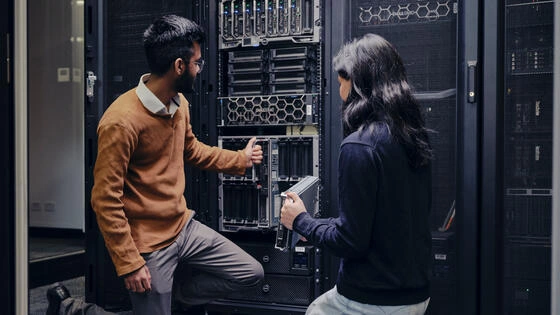 Two master of cyber security professional students lean down and look at computer servers. 