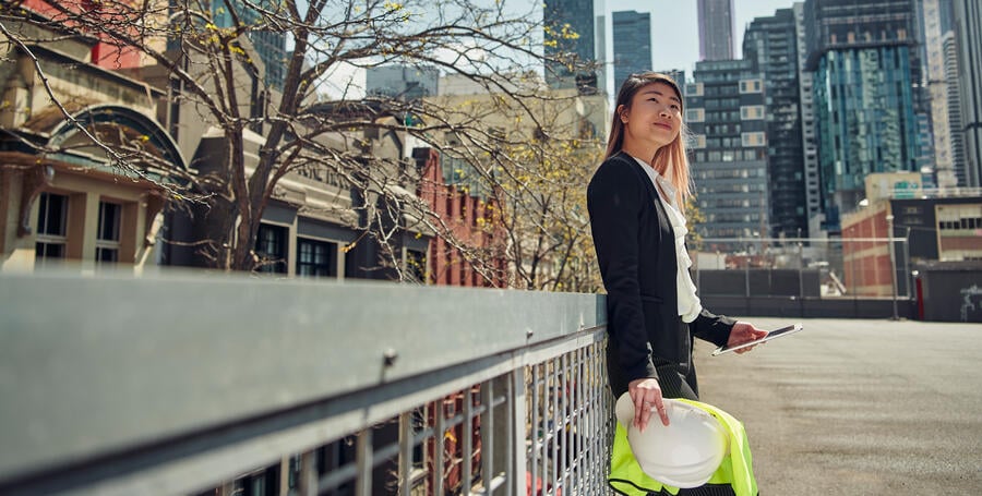 A woman stands holding a tablet and a construction hard hat.