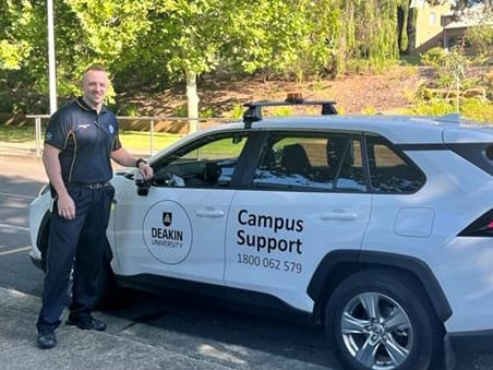 Campus support officer standing next to car on campus