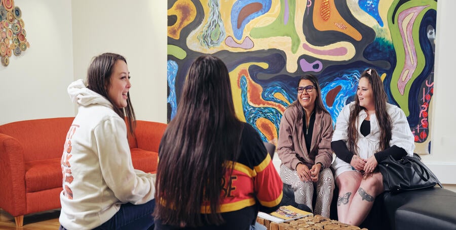 Four students sit in a circle talking at the NIKERI Institute, Deakin University. A colourful painting in the background. 