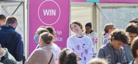 A staff member stands in front of a pink sign at Deakin Open Day.