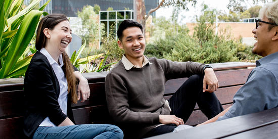 Three students sitting on benches outside talking