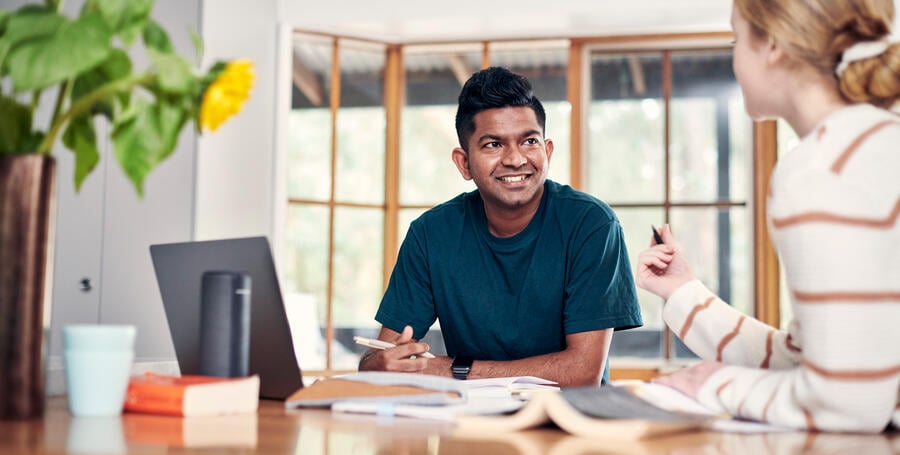 A student studies at a dining table with a laptop and books. 