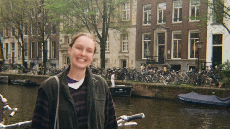 Student standing in front of bikes and a river in Amsterdam