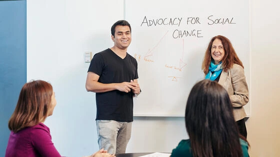 Two deakin master of health promotion student teachers present on a whiteboard to others in a classroom.