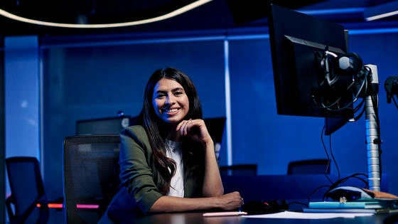 Deakin master of data science sitting at table with computer and smiling on campus.