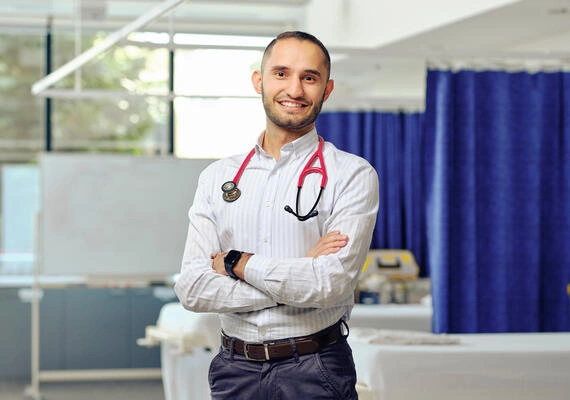Medicine student Mo Al-Ameri stands in a hospital room with a stethoscope around their neck.