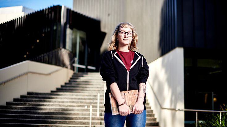 Student standing outside Burwood building holding a laptop