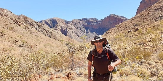 Craig standing among yellow grass and red mountains in the central Australian bushland
