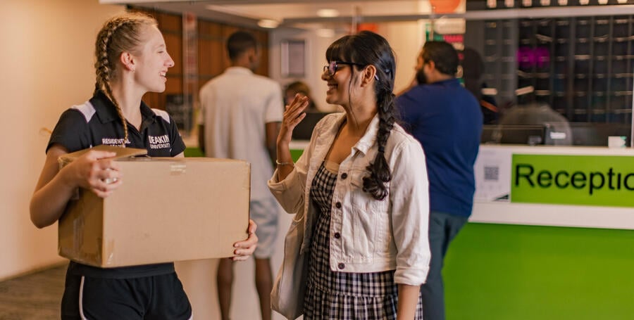 A staff member holding a box speaks with an international student in the reception area of Deakin Res. 