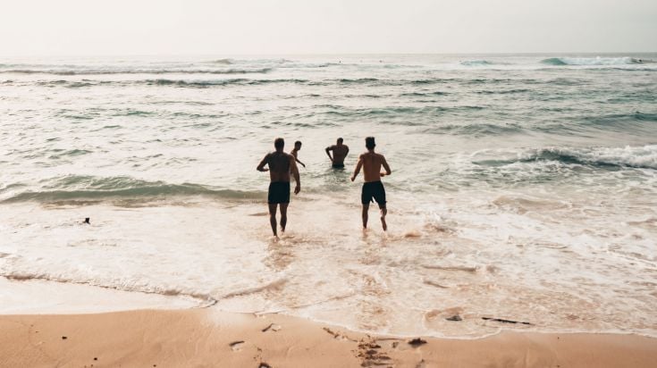 Four young people entering the ocean for a swim