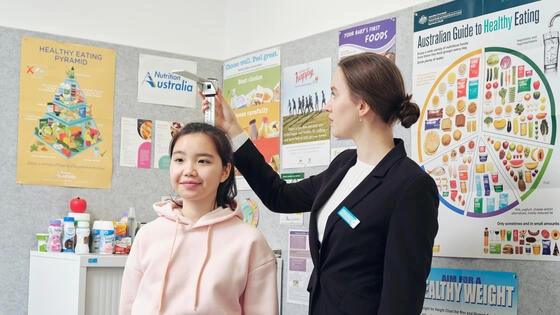 Deakin master of dietetics student measures height of patient in medical office with nutrition posters.