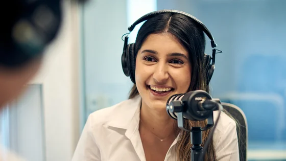 Deakin bachelor of communication students wearing headphones sit at table with microphone.