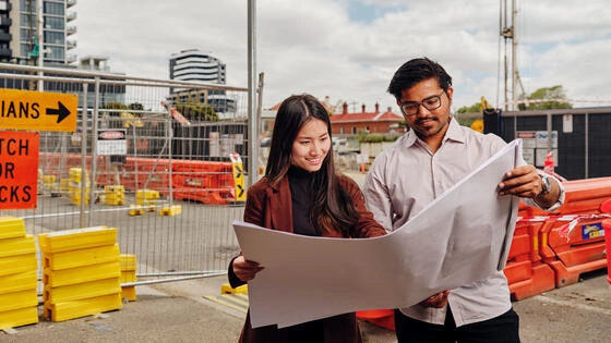 Two Deakin graduate diploma of construction management students look at plans on a construction site.