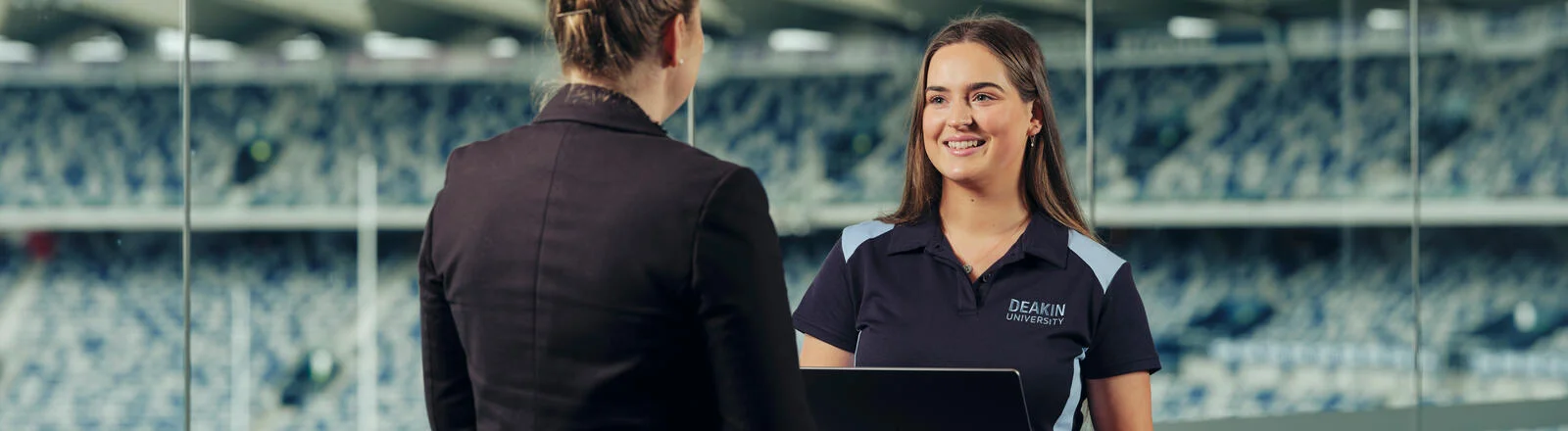 Two Deakin exercise and sport science/business students chat in a stadium.