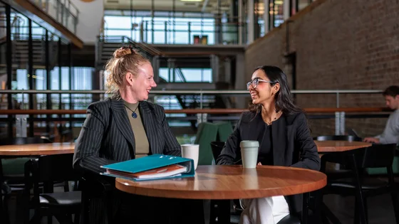 Two students sit at a table with coffees.