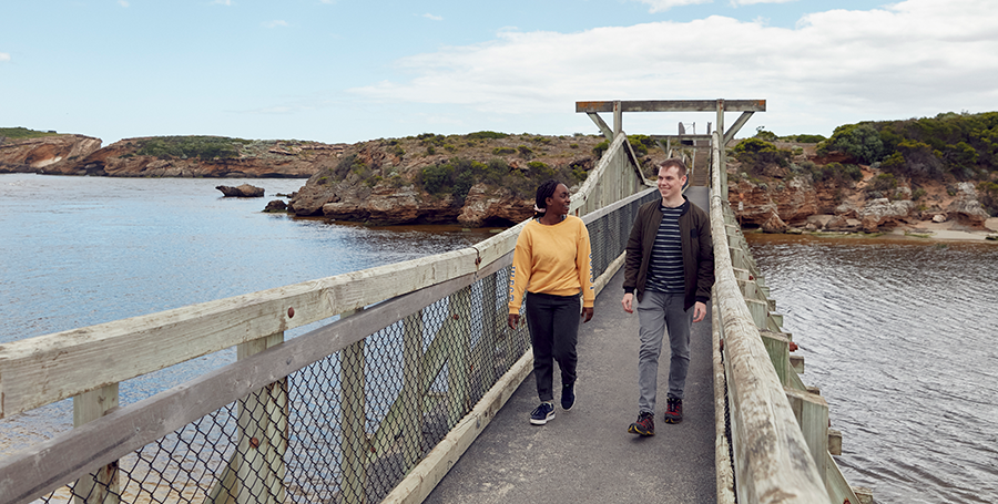 Two students crossing a bridge over a river