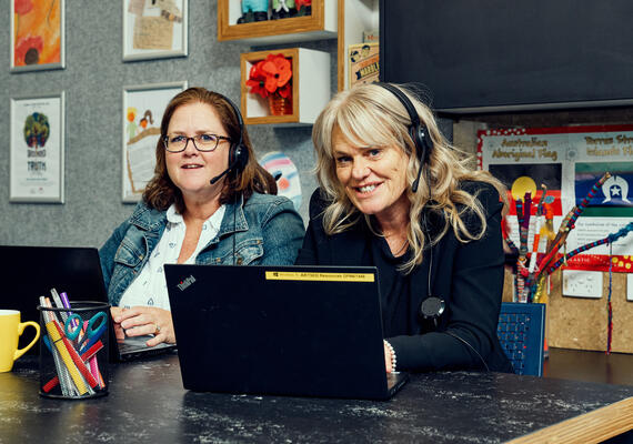 Two educators in classroom wearing headsets.