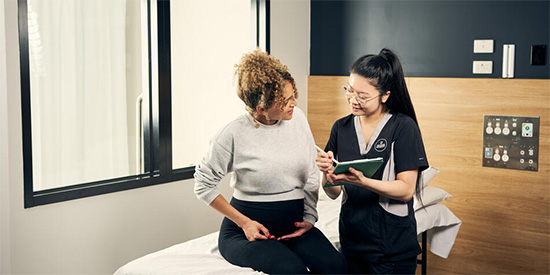 Deakin nursing student and patient sitting on a hospital bed.
