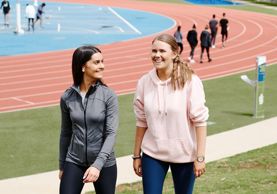 Two students walking and smiling together near a running track at Deakin Geelong Waurn Ponds campus