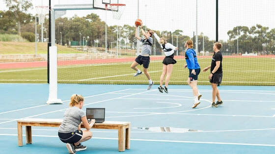 A Deakin postgraduate sport performance analysis student watches a group of students play basketball. 