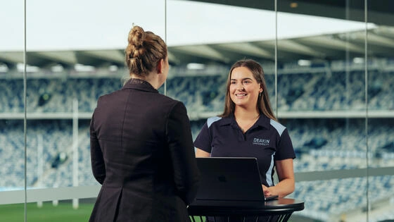 Two Deakin exercise and sport science/business students chat in a stadium.
