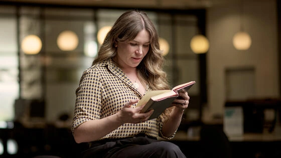 Deakin graduate diploma of writing and literature student reads book whilst leaning on table on campus.