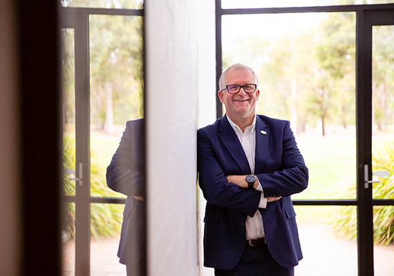 Vice-Chancellor Professor Iain Martin stands smiling with his arms crossed in front of a window.