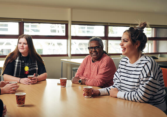 Three Deakin students sit at a table talking at the NIKERI Institute.