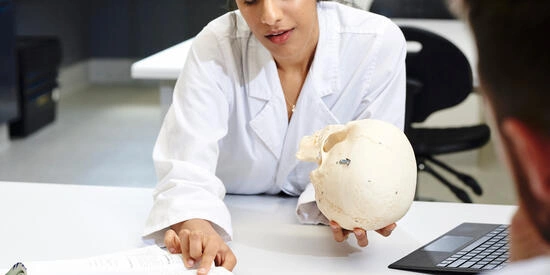 Deakin University student pointing at a textbook with a skull model