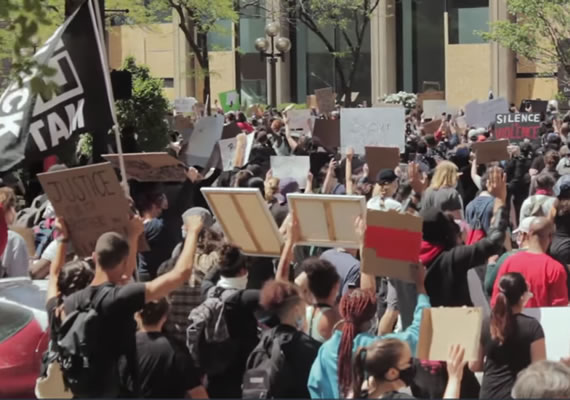 Politics and policy studies video still depicting a large group of people attending a protest in a city.