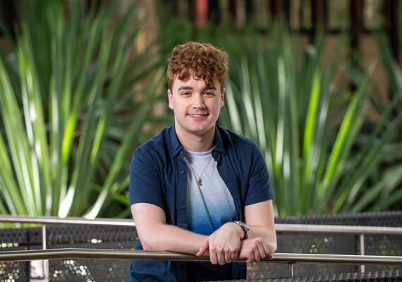 Deakin Accelerate student Michael Killen leans against a handrail with a leafy green background