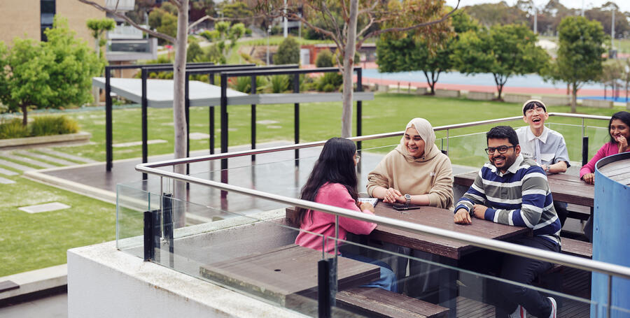 A group of Deakin students socialise at the picnic tables of a Waurn Ponds campus cafe