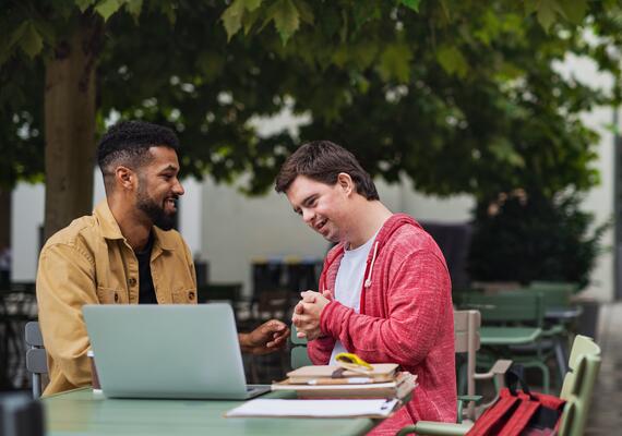 Two people sitting at a table with a laptop and notebook on campus.
