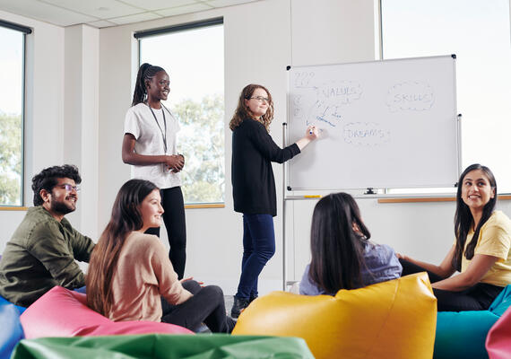 A group of Deakin students sit on bean bags around a whiteboard 