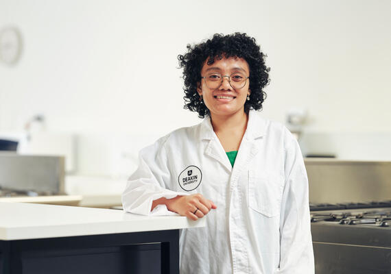 Bachelor of Nutrition Science student, Safira, wears a white coat and stands in a kitchen.