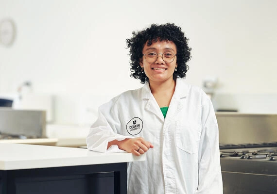 Bachelor of Nutrition Science student, Safira, wears a white coat and stands in a kitchen.