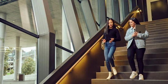 Two Deakin students talking and walking down stairs.