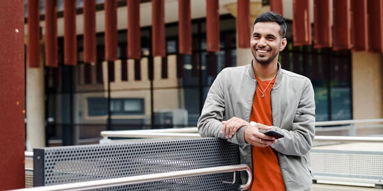 A student outdoors on a Deakin campus, smiling and holding a mobile phone