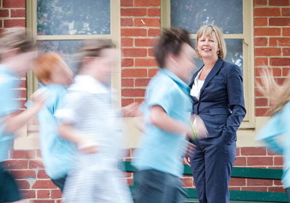 School teacher in yard with students running past
