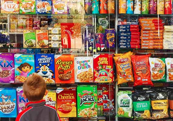 A young child stands in front of a supermarket wall of sugary cereal boxes.