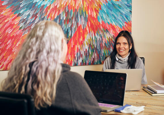 Deakin student receiving research support at table on campus with colourful painting on wall.